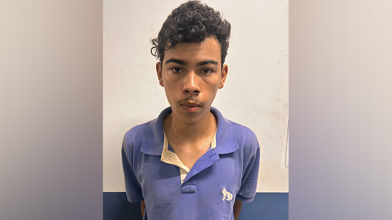 Jovem de pele parda, com cabelo cacheado escuro, vestindo camisa polo azul contra um fundo de parede neutra.