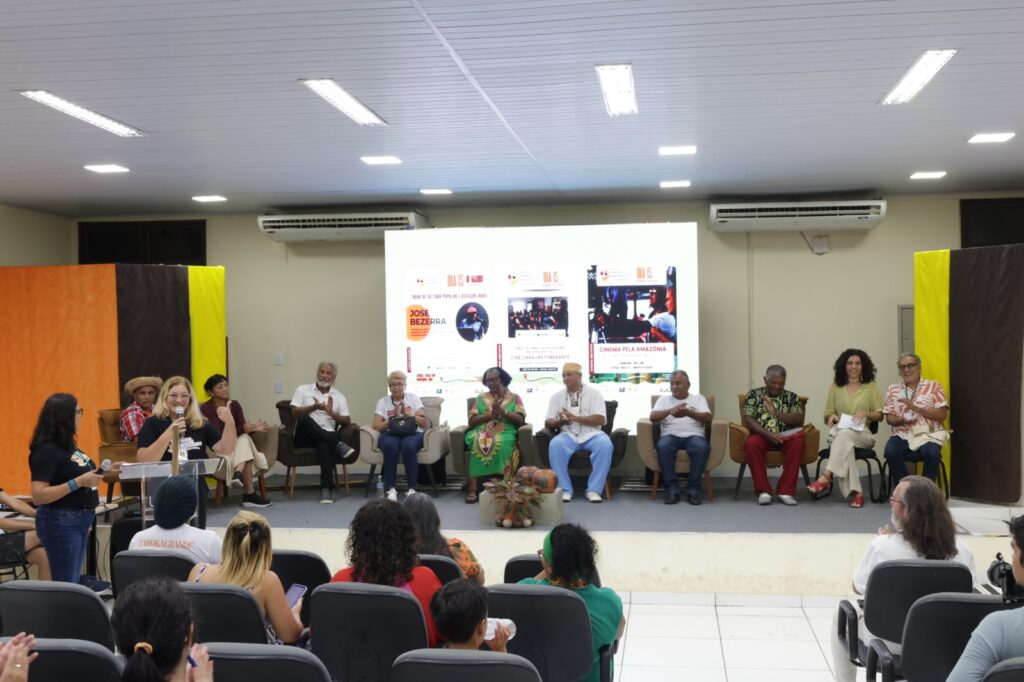 Painel de palestrantes sentados em um palco em frente a uma tela de projeção com o tema 'Dia 15'.