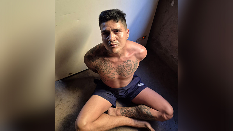 Homem jovem tatuado sentado no chão com braços cruzados atrás das costas.