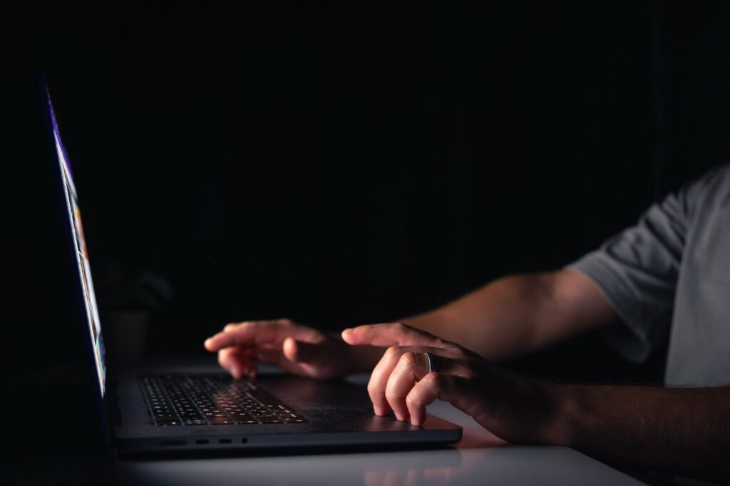 Mãos digitando em um laptop em ambiente escuro