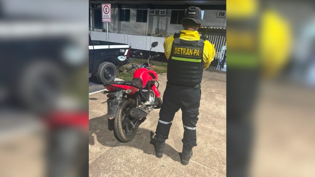 Agente do DETRAN-PA de costas usando colete reflexivo ao lado de uma motocicleta vermelha