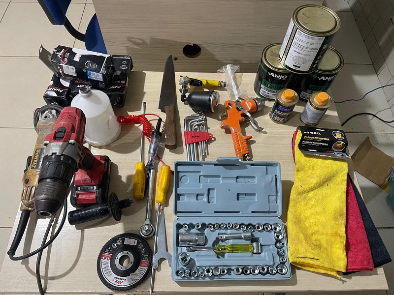 Conjunto de ferramentas manuais e elétricas, produtos químicos e acessórios de oficina espalhados sobre uma mesa.