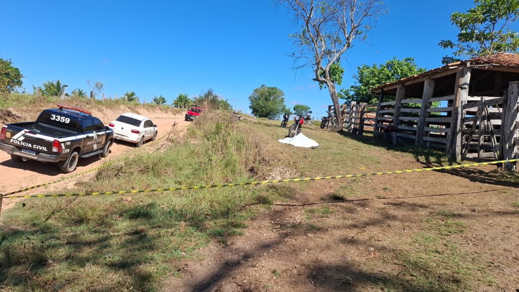 Cena de acidente em estrada rural com carro branco, motocicletas e fita de isolamento amarela.