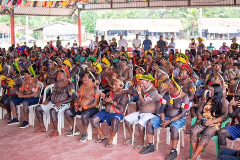 Grupo de indígenas sentados em cadeiras de plástico em um galpão aberto durante uma reunião.
