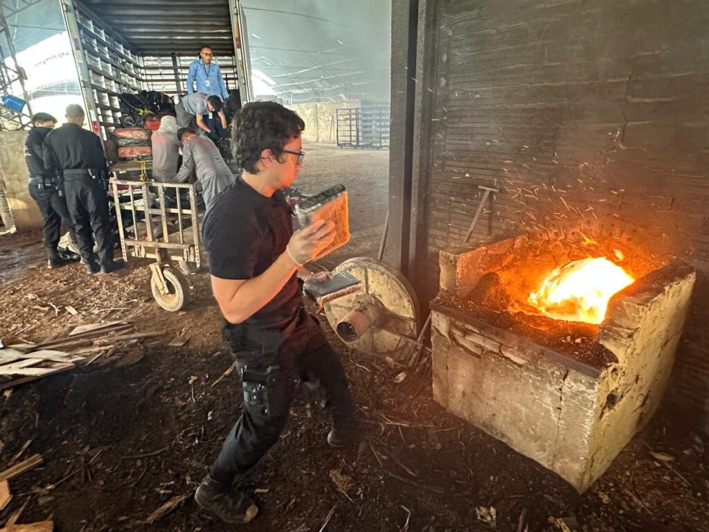 Homem de óculos jogando pacotes em uma fornalha industrial acesa.