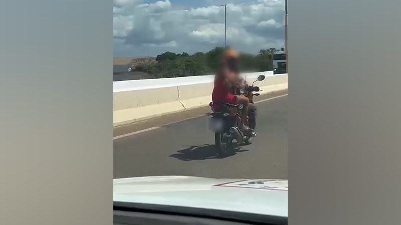 Pessoa vestindo uma peça de roupa vermelha andando de moto em uma rodovia.
