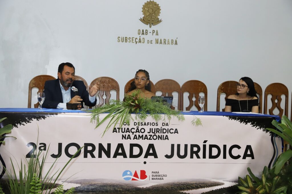 Três pessoas sentadas em uma mesa de conferência sob o banner da Jornada Jurídica na OAB Marabá.