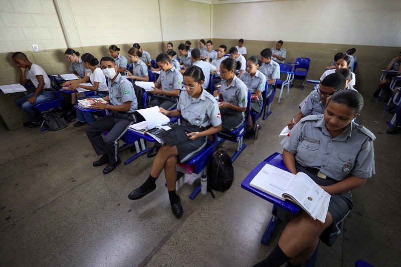 Alunos em uma sala de aula utilizando uniformes escolares com brasões.