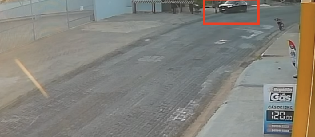 Carro branco trafegando em uma rua de asfalto com marcas de frenagem.