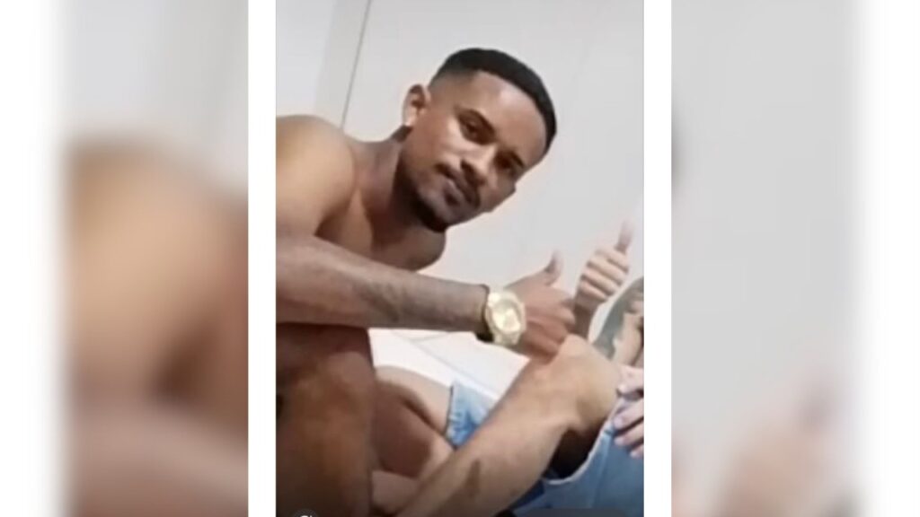 Jovem homem de pele parda sem camisa, usando relógio dourado, fazendo sinal de positivo para a câmera.