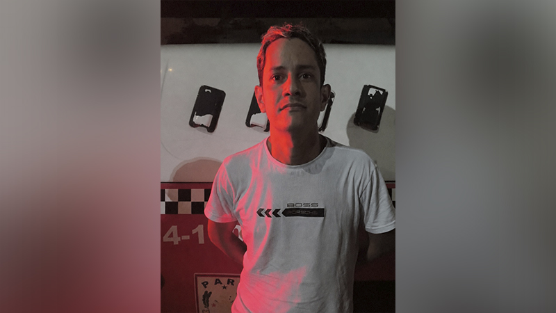 Homem de camiseta branca com estampa da Porsche posando em frente a um veículo oficial.