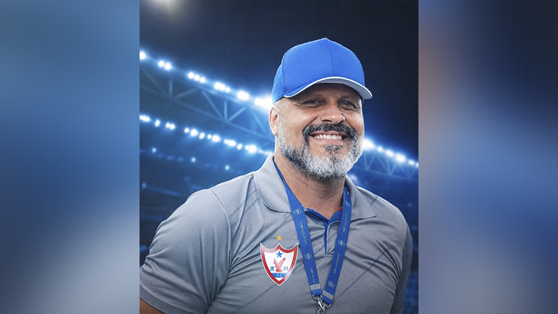 Treinador de futebol barbudo sorrindo com boné azul e camisa cinza do América Mineiro.