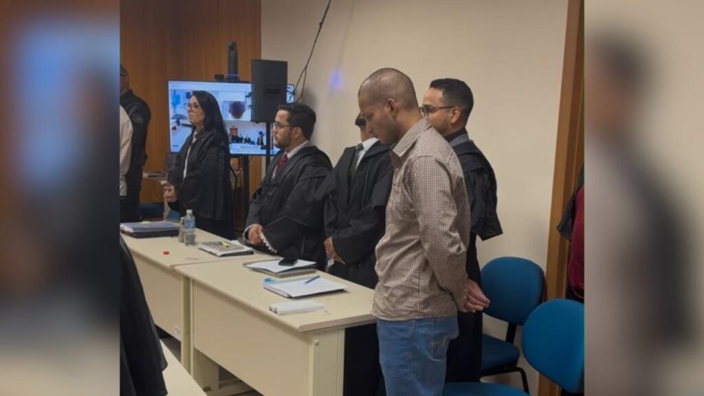 Homem em pé diante de mesa de tribunal com advogados e juíza ao fundo