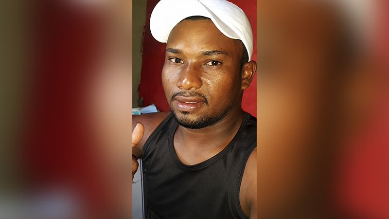 Retrato de um homem jovem de pele negra usando boné branco e regata preta.