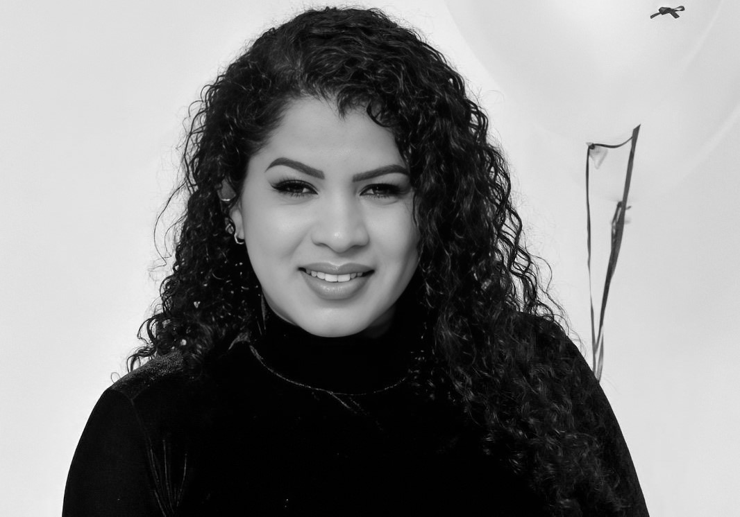 Retrato em preto e branco de uma mulher jovem com cabelos cacheados sorrindo.