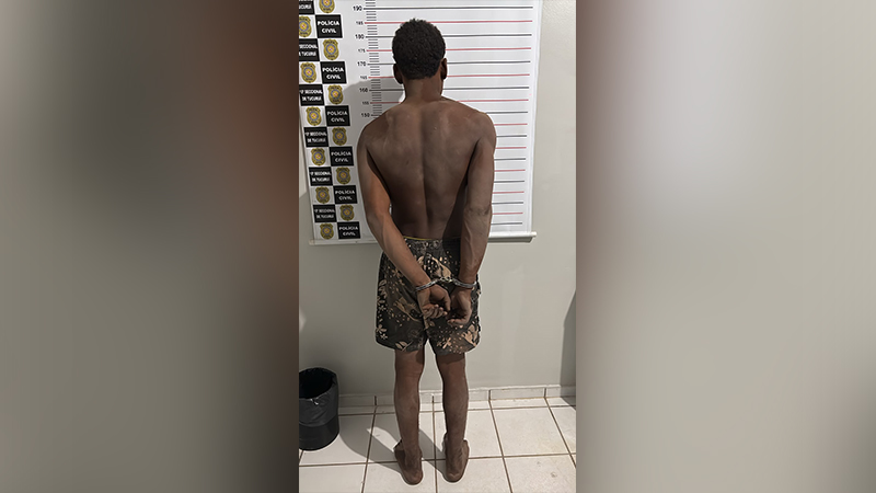 Homem sem camisa algemado de costas diante de uma régua de medição da Polícia Civil.