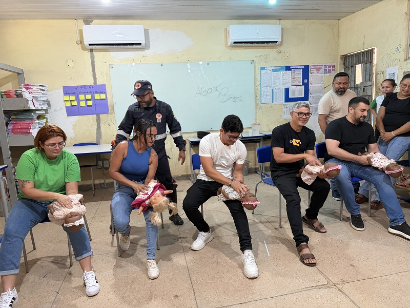 Grupo de pessoas participando de um treinamento de primeiros socorros em bebês com bonecos em uma sala de aula