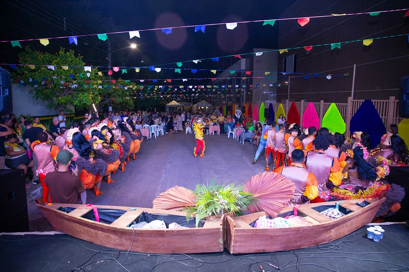 Dançarinos de quadrilha em apresentação noturna ao ar livre decorada com bandeirinhas.