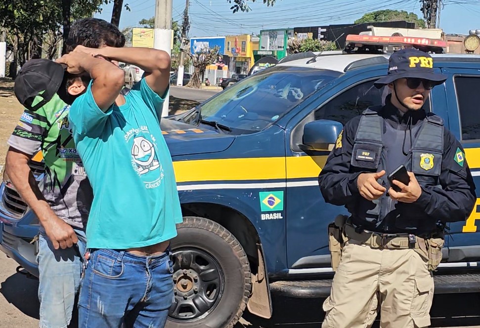 Homem com as mãos na cabeça sendo abordado por policial rodoviário federal.