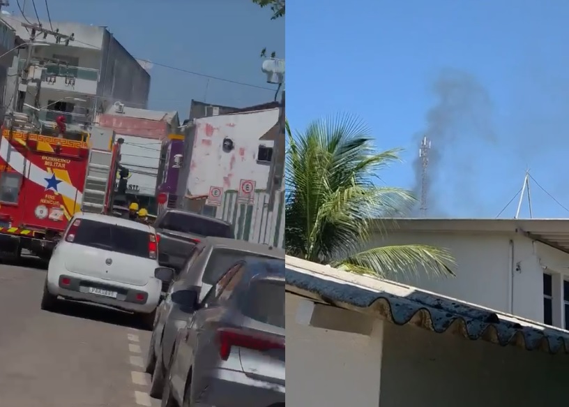 Caminhão do corpo de bombeiros parado em rua movimentada e fumaça subindo perto de uma torre de antena.