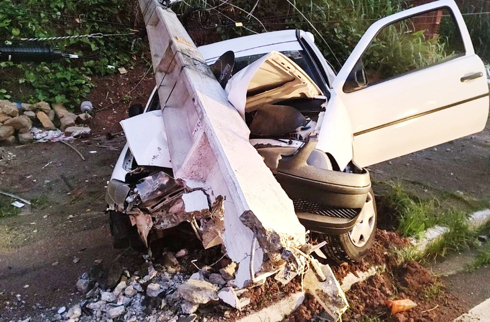 Carro branco batido contra um poste de energia elétrica caído no chão.