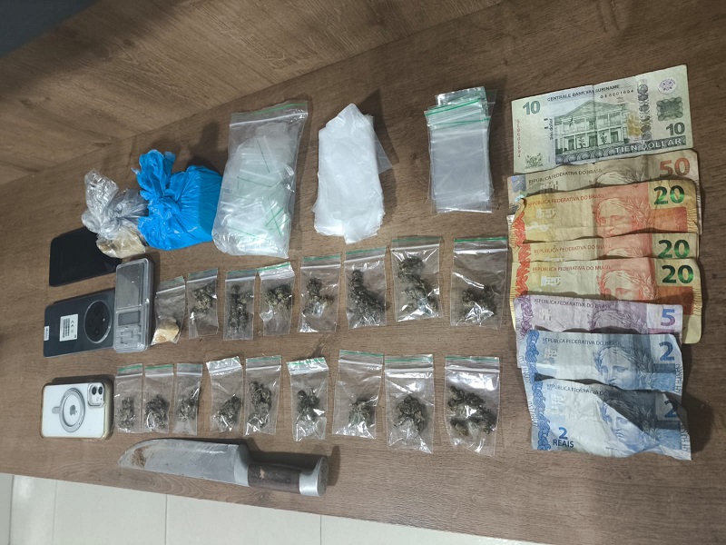Apreensão de drogas, dinheiro, celulares e uma faca sobre uma superfície de madeira.