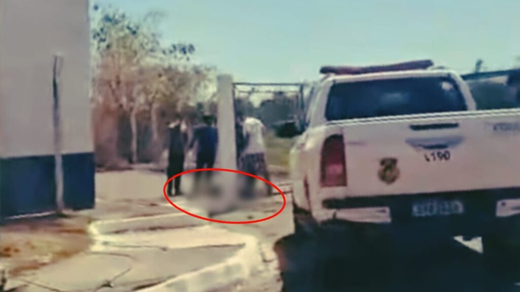 Pessoas em pé ao lado de um veículo policial, com área censurada em destaque