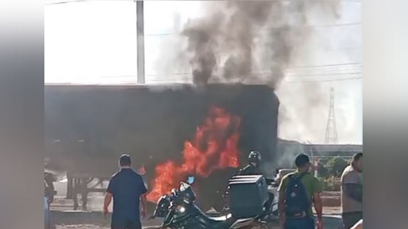 Caminhão em chamas em uma via pública com pessoas observando e uma motocicleta próxima