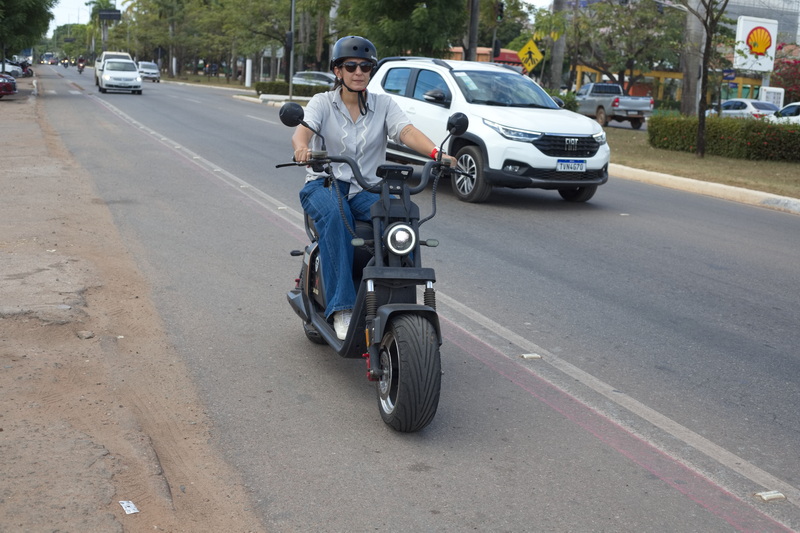 Mulher pilotando uma scooter elétrica preta em uma avenida movimentada.