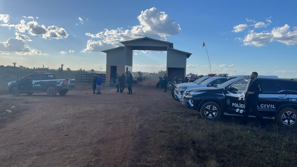 Viaturas da Polícia Civil paradas na entrada de uma propriedade rural com agentes em serviço.