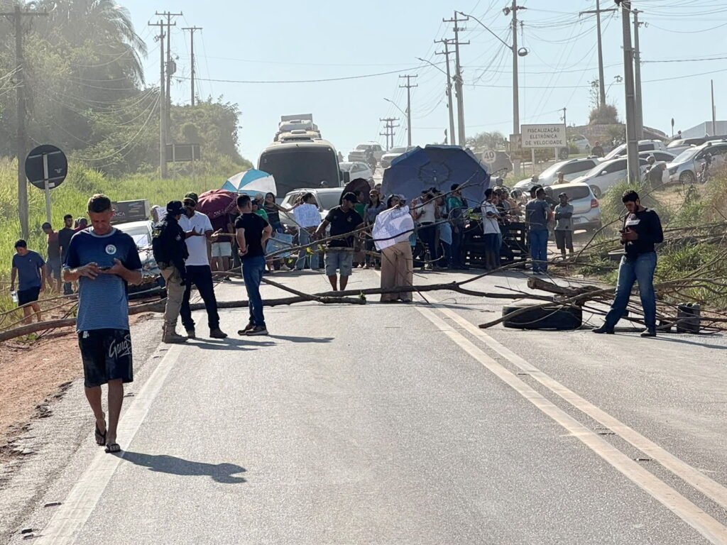 Grupo de pessoas realizando bloqueio em uma rodovia com galhos de árvores e guarda-sóis.