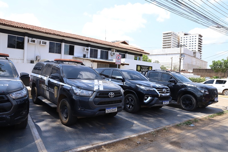 Viatura da Polícia Civil estacionada em frente a prédio administrativo sob o sol.