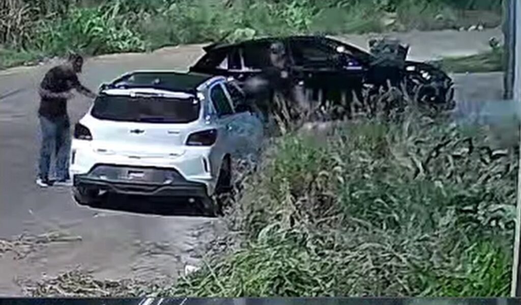 Carro branco Chevrolet Onix estacionado em estrada de terra cercada por vegetação.