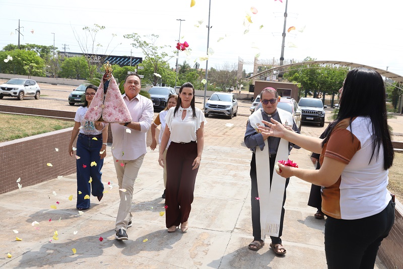 Grupo de pessoas caminhando ao ar livre carregando uma imagem de Nossa Senhora sob chuva de pétalas de flores