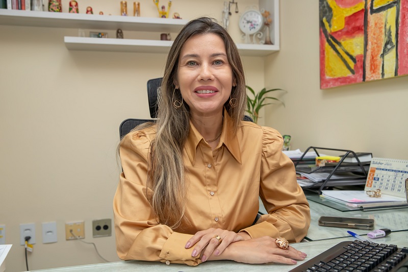 Mulher de cabelos longos e castanhos sorrindo sentada em sua mesa de escritório