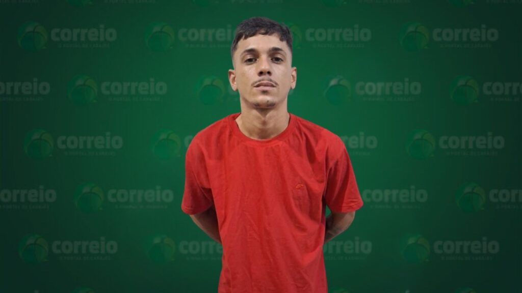Jovem de pele clara, cabelo curto escuro e camiseta vermelha em frente a fundo verde com logomarca.
