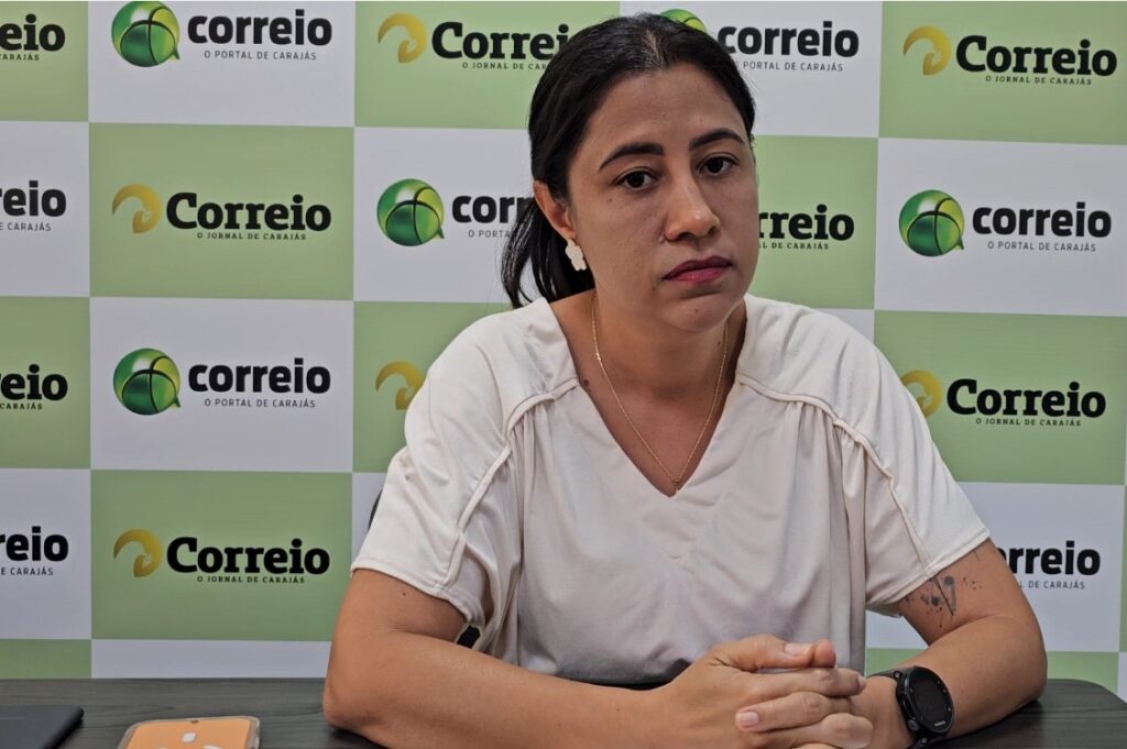 Mulher de pele clara, cabelos escuros presos e blusa branca, posando em frente a painel com a logo do Correio do Carajás.