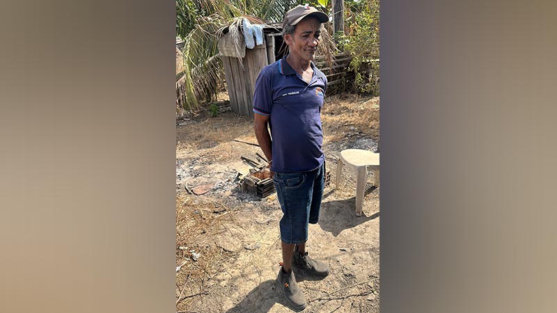 Homem de meia-idade vestindo boné, camisa polo azul e calça jeans em uma área rural.