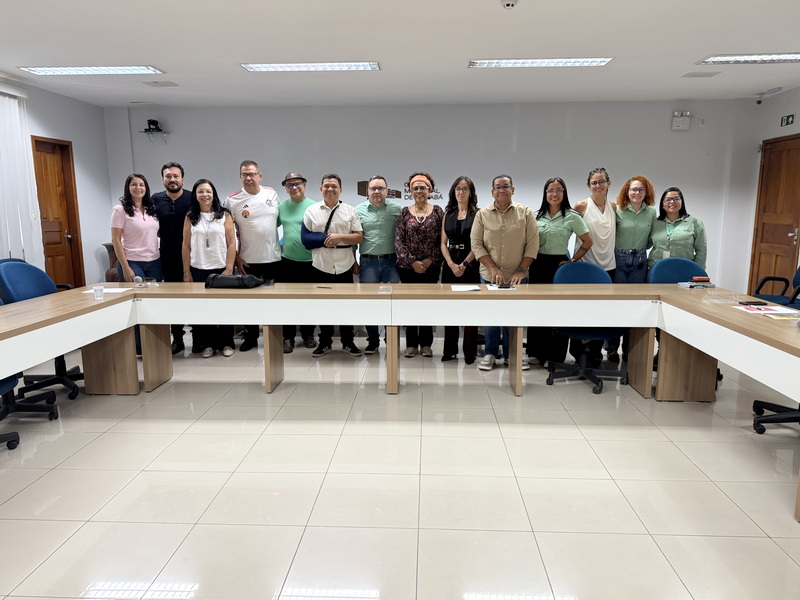 Grupo de quinze pessoas posando para foto em sala de reunião com mesa grande em forma de U.