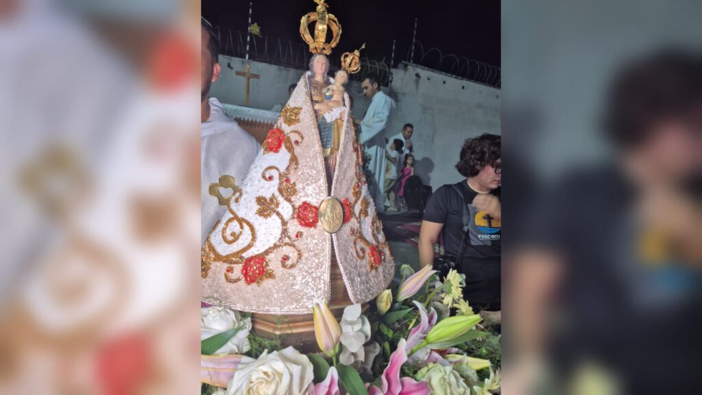 Imagem de Nossa Senhora de Fátima ornamentada com flores em uma procissão religiosa à noite