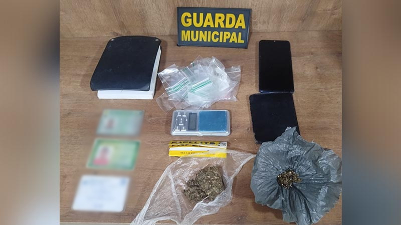 Itens apreendidos pela Guarda Municipal incluindo drogas, balança de precisão, celular e documentos.
