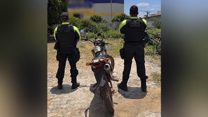 Dois agentes de trânsito em pé atrás de uma motocicleta em uma área aberta.