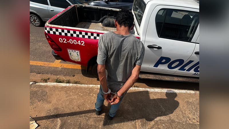 Homem algemado ao lado de uma viatura da Polícia Militar do Pará.
