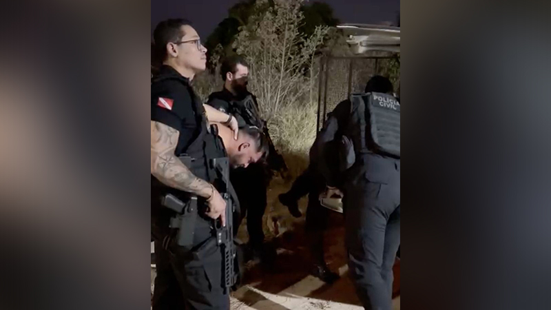 Policiais civis realizando a detenção de um suspeito à noite em área de mata.
